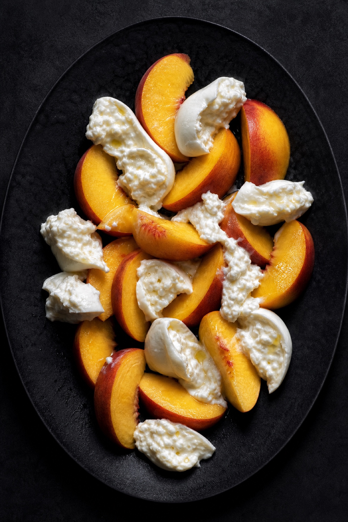 Sliced yellow peaches and torn burrata on a dark platter, overhead flat-lay, vegetarian gluten-free