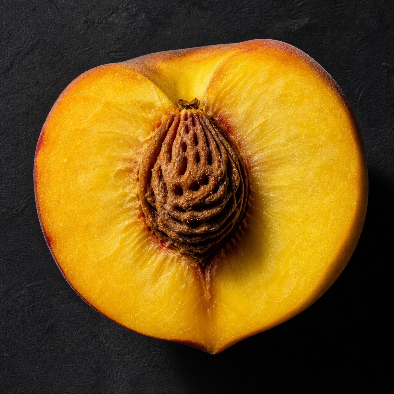 Sliced yellow peach showing the stone, macro flat-lay with hard side light